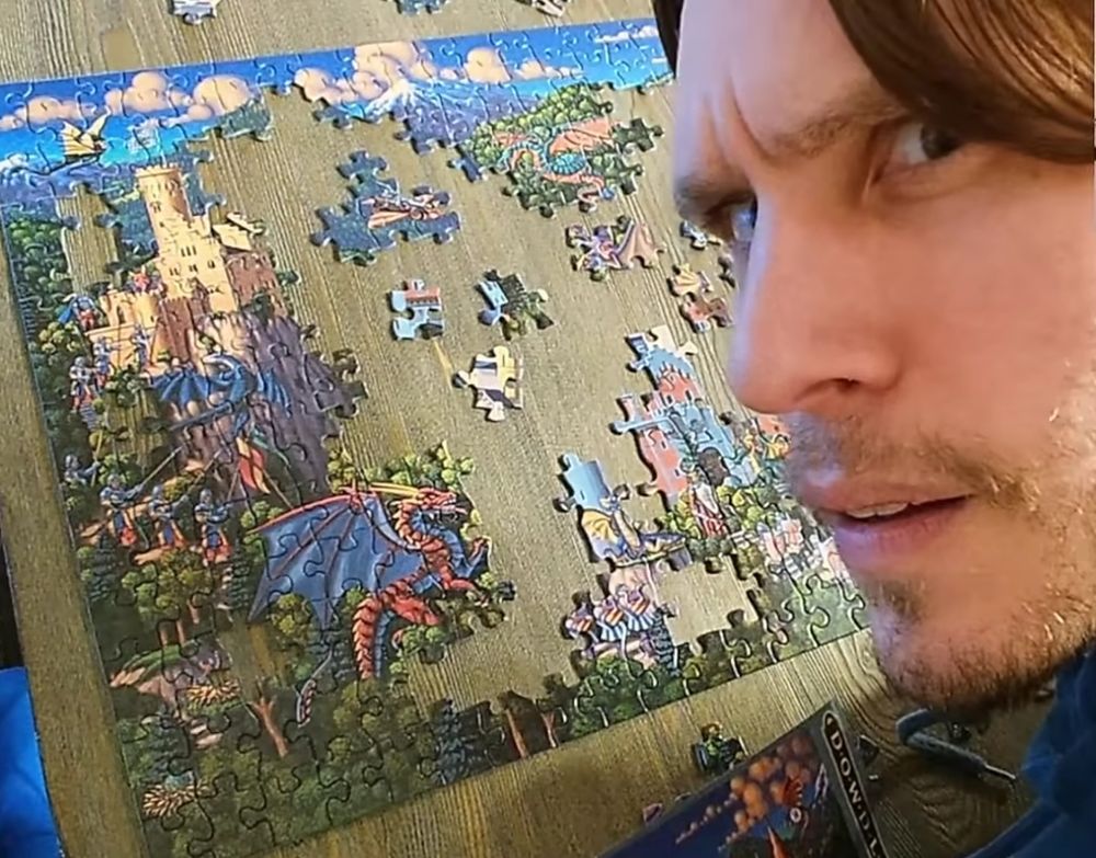 Jerma leaning into frame from the left, giving a quizzical look at the camera. Behind him is a partially completed puzzle. 