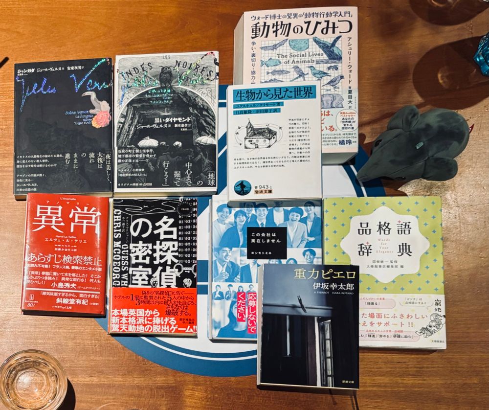 机の上に9冊の本が並んでいる画像です。本のタイトルは「異常/アノマリー」、「名探偵の密室」、「黒いダイヤモンド」、「ジャンガダ」、「ウォード博士の驚異の「動物行動学入門」動物のひみつ」、「生物から見た世界」、「この会社は実在しません」、「重力ピエロ」、「品格語辞典」です。