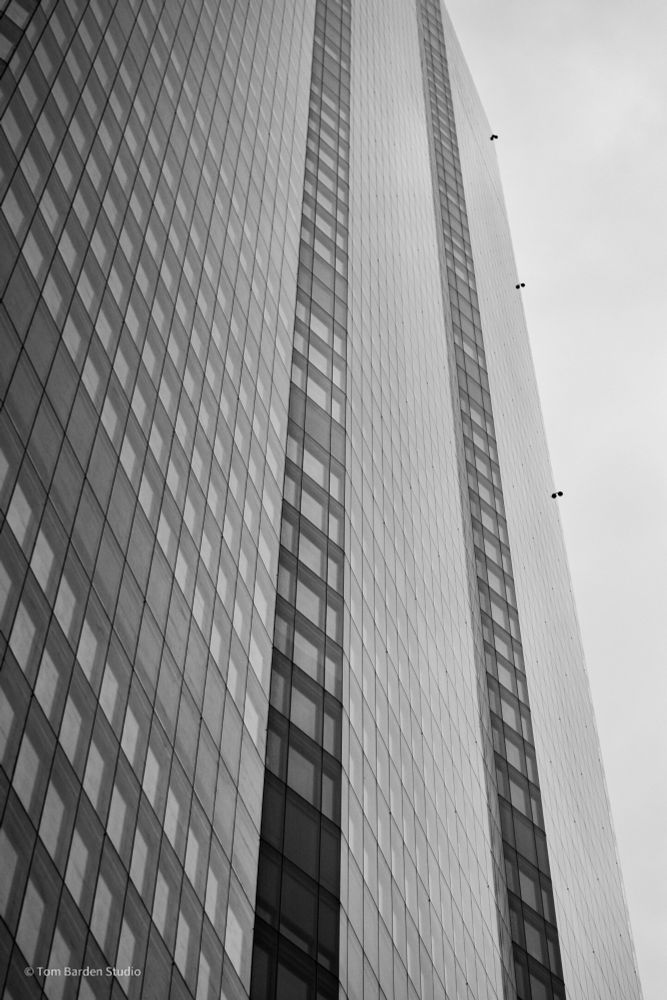 A skyscraper rises towards the sky. It is cropped off the tip of the photograph. Black and white study.