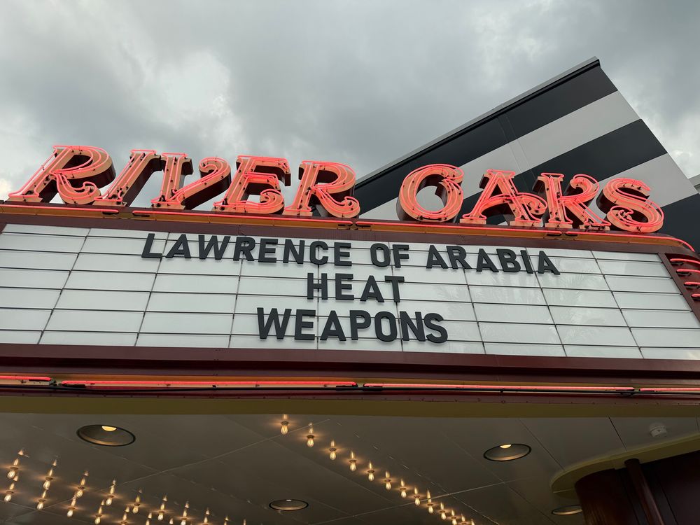 A sign on the exterior of the Rover Oaks Theater advertising three movies - Lawrence of Arabia, Heat and Weapons - or one amazing sequel - Lawrence of Arabia: Heat Weapons. 