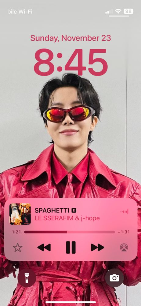 J-Hope in a red shirt, red tie, and red long, belted trench coat, wearing sunglasses and reading to hit the stage for his solo tour