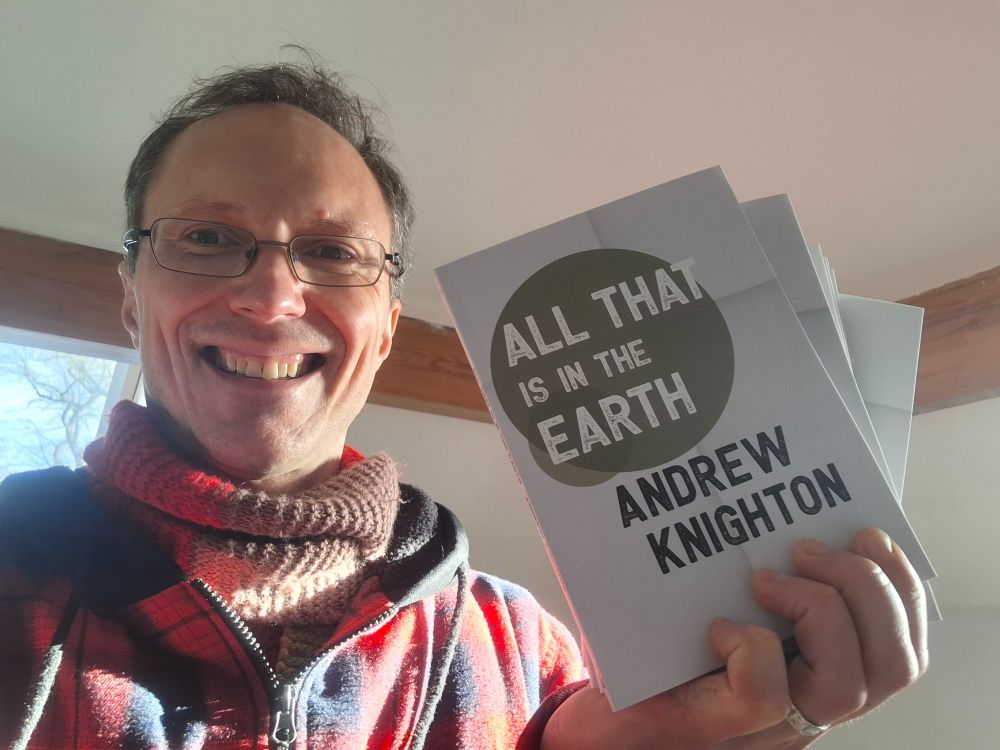 An author holding up paperback copies of his book - All That Is in the Earth by Andrew Knighton