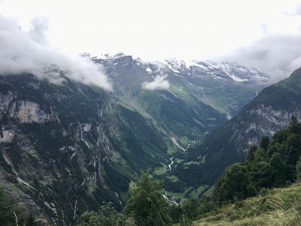 A view from above of a deep Swiss valley, surrounded by snow-and-cloud capped mountains.