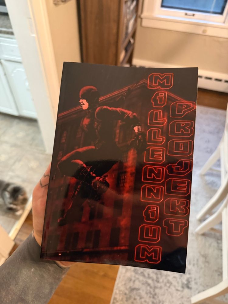 A hand holding the TTRPG gamebook “Millennium Projekt”. A cat is in the background. 