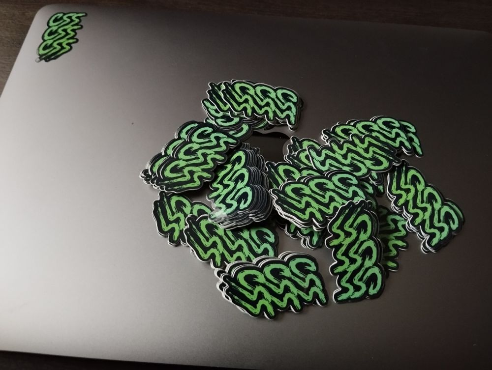 A brand new macbook with one CSS sticker in the top left corner of the cover and dozens more of the same stickers lying on top of the same cover.