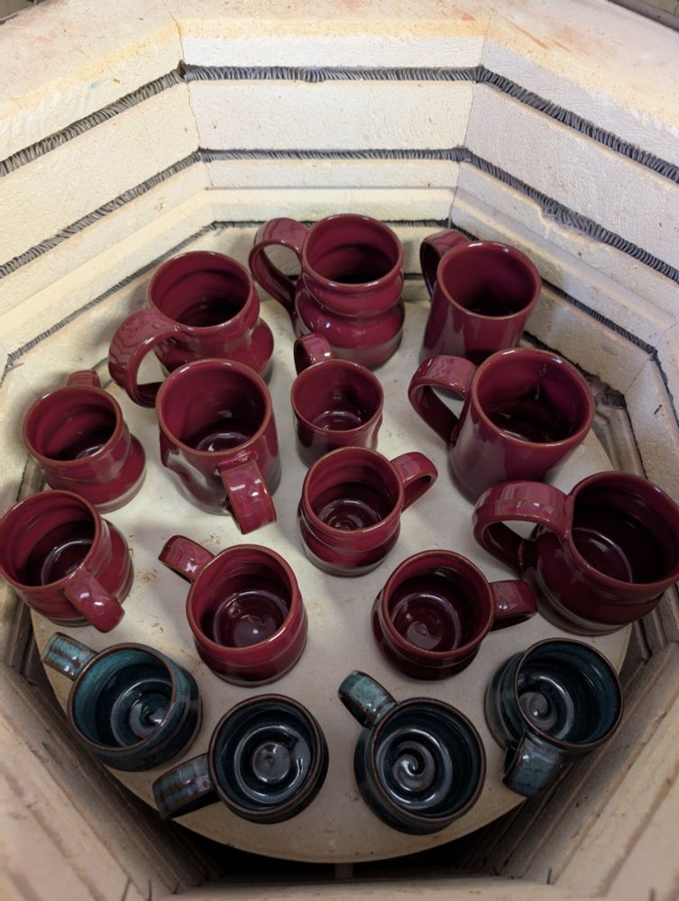 The inside of an electric pottery kiln, the shelf full of red and blue mugs. 