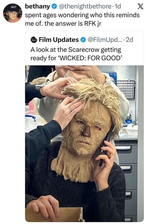 A tweet from bethany saying she spent ages wondering who the pictured person reminds her of, concluding it's RFK Jr. The picture shows an actor wearing a partially completed Scarecrow mask from Wicked, with the mask pulled over their head while they hold a phone to their ear as makeup artists work on the mask.
