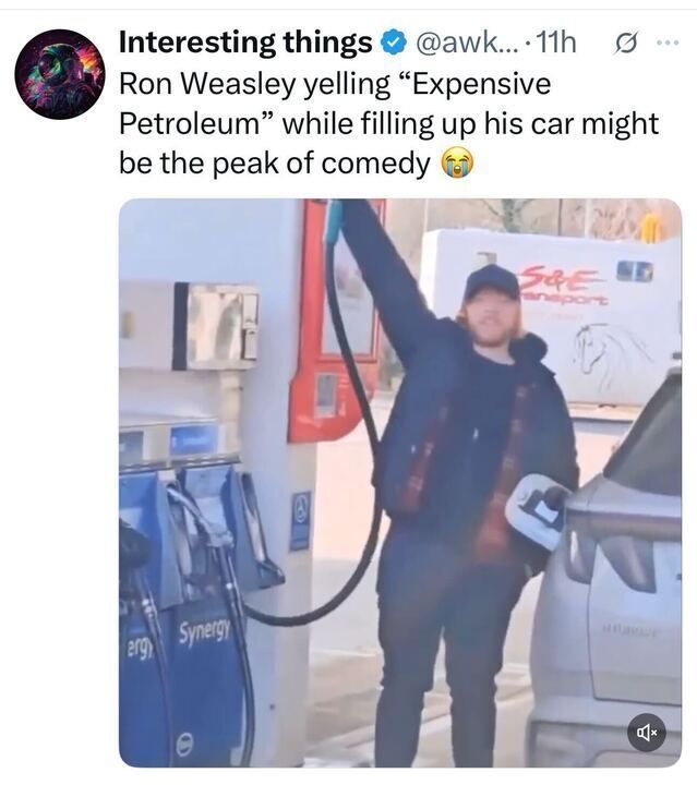 A screenshot of an X post by @awk
.... from 11 hours ago, with the username "Interesting things" and a colorful profile picture. The post humorously states, "Ron Weasley yelling 'Expensive Petroleum' while filling up his car might be the peak of comedy ." The attached image shows a person resembling Ron Weasley from Harry Potter, wearing a cap and dark jacket, raising one arm dramatically while holding a gas pump nozzle in the other hand, fueling a car at a station with "Synergy" pumps and a truck in the background.
