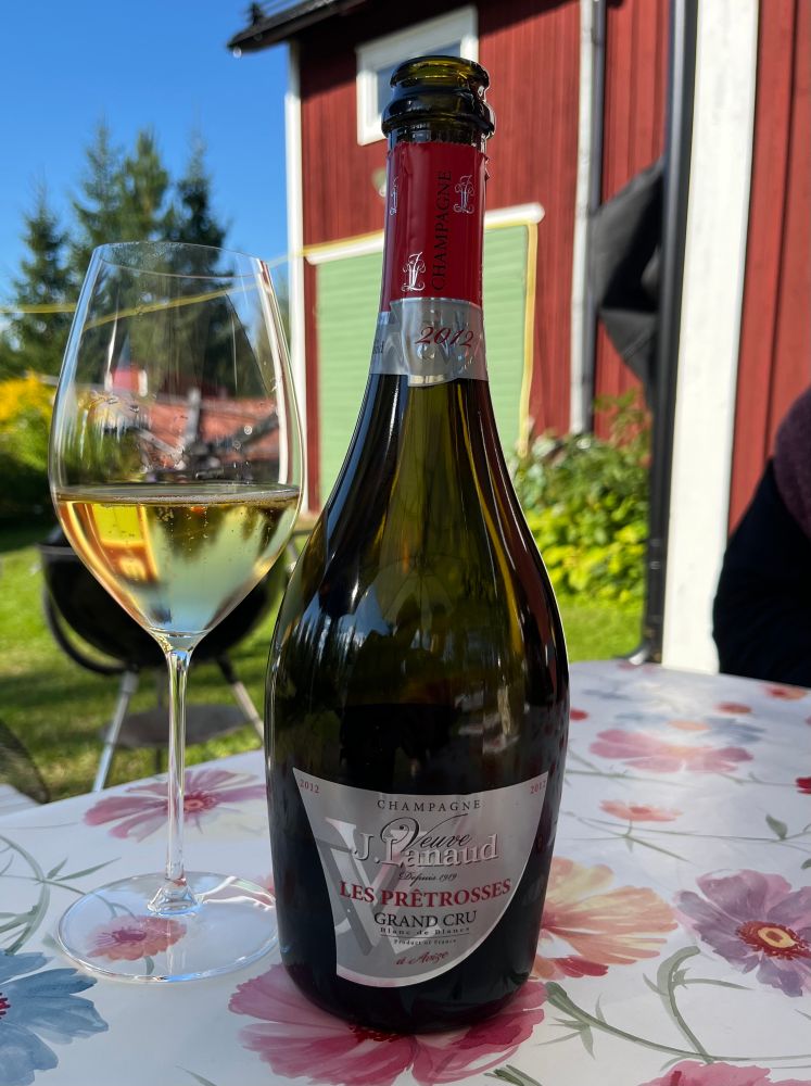 En flaska champagne och ett upphällt glas på en blommig duk. 