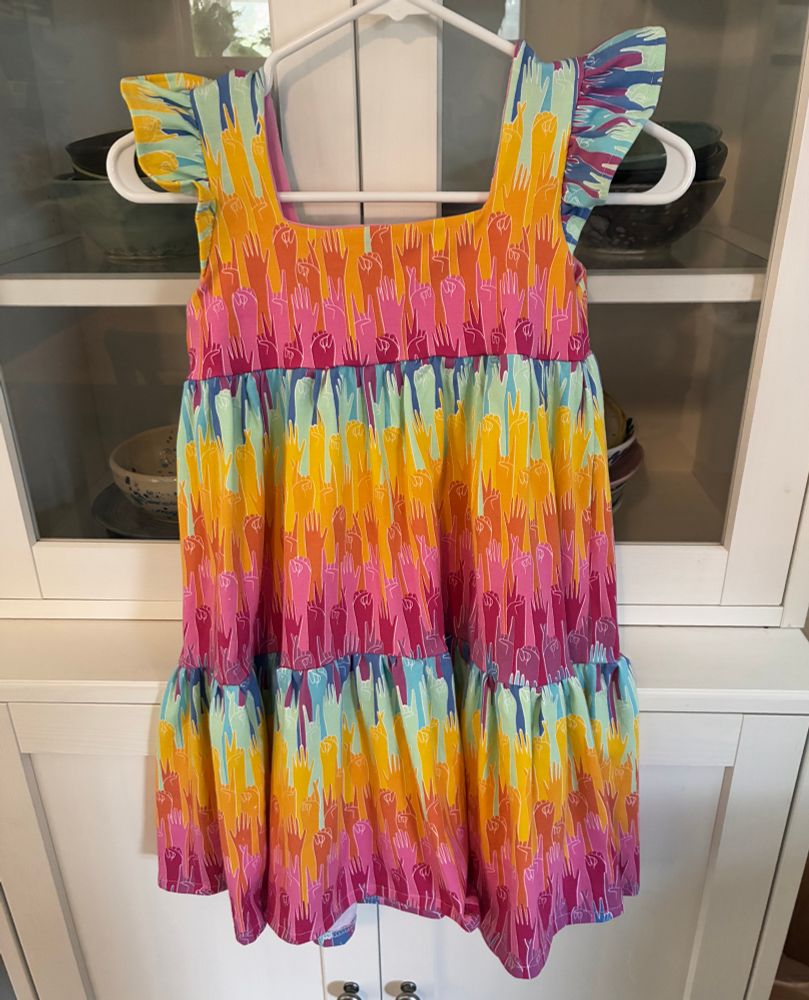 Babydoll style dress with a ruffle bottom, pattern is upraised hands in rainbow ombre making signs like peace, resistance, love