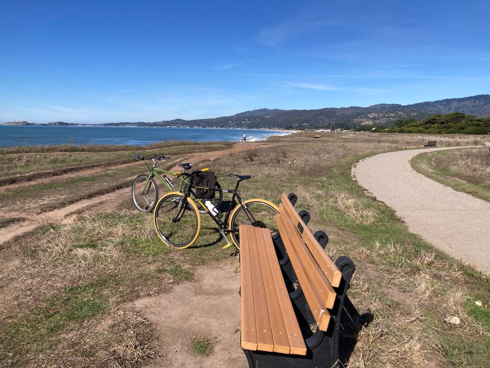 Two bikes next to a bench along a coastside trail.  