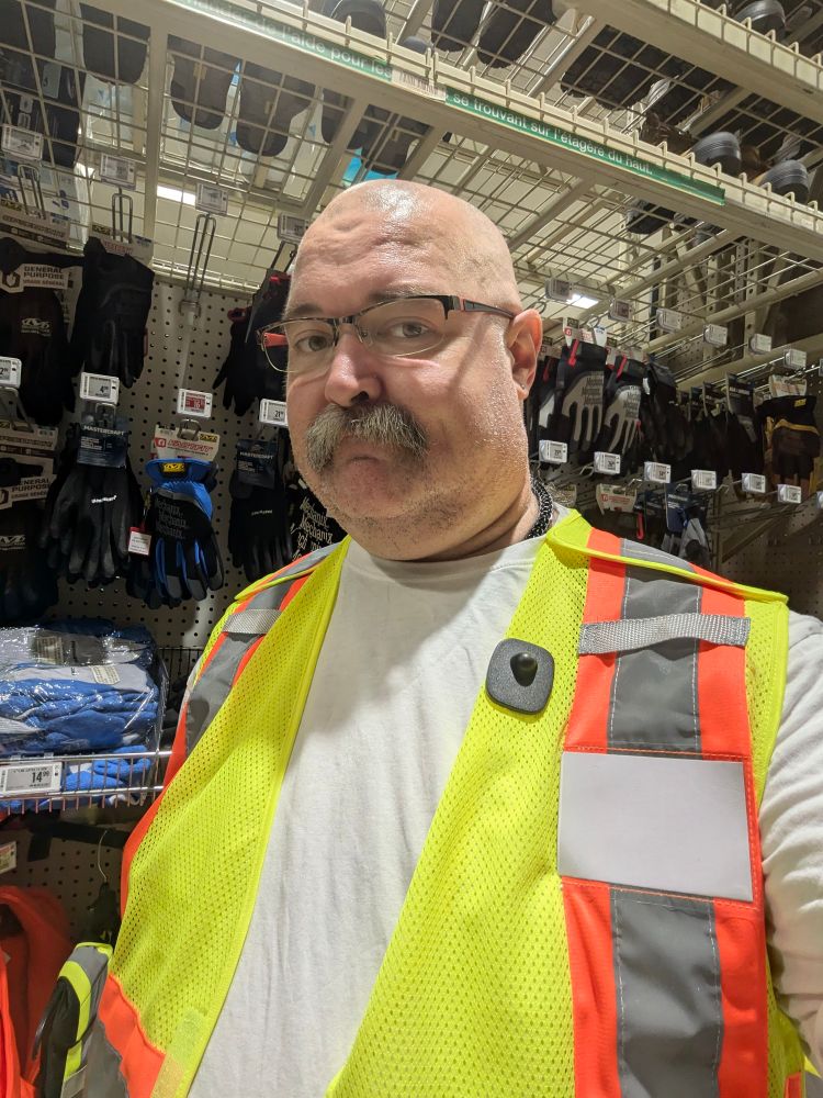 A fat, mustachioed man in a white t shirt and reflective safety vest