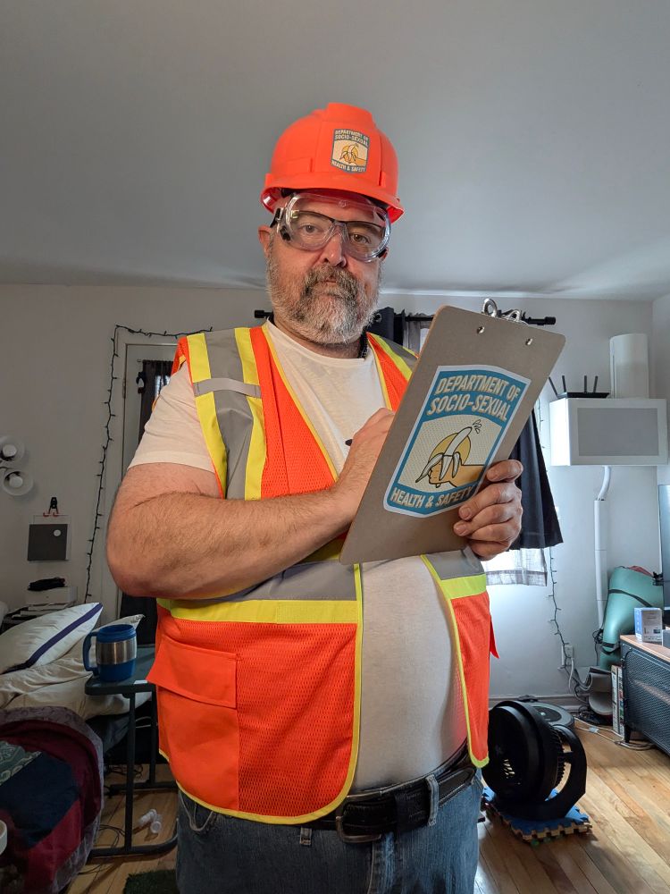 A fat man in jeans, a white t shirt, a high vi visibility orange vest and hard hat holding a clipboard. The logo on the hat and clipboard say "Department of Socio-Sexual Health And Safety" and there is a picture of a hand holding a sweaty banana.