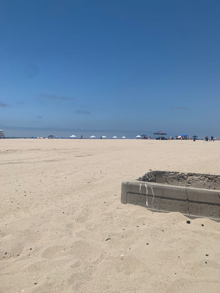 A wide beach. In the distance: umbrellas, ocean. In the foreground: the fire pit i must defend 