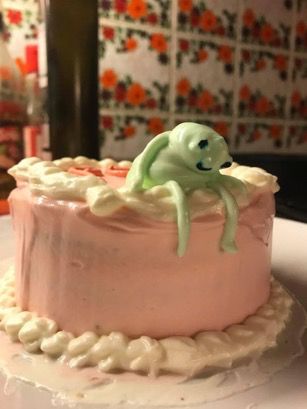 A green frosting frog sits atop a green cake, slumped but smiling