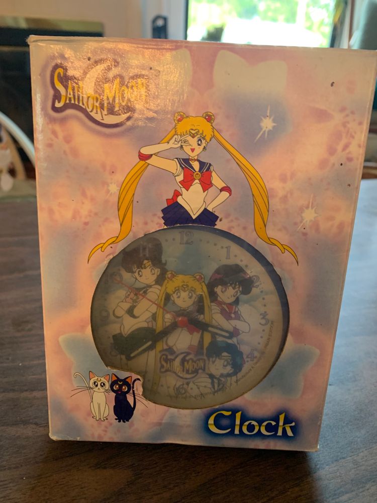 A sailor moon alarm clock from the 1990s in its original box. Artemis and Luna are on the box, along with sailor moon herself. Inside, the alarm clock face shows the sailor scouts 