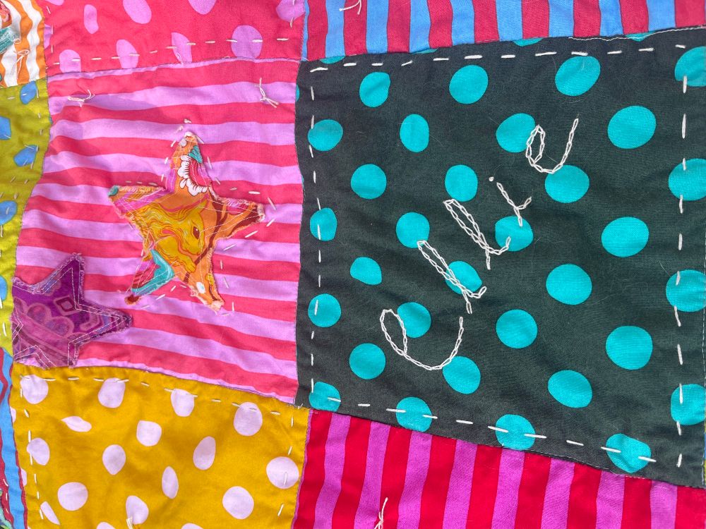 Embroidered name Elllie on turquoise and dark gray fabric.