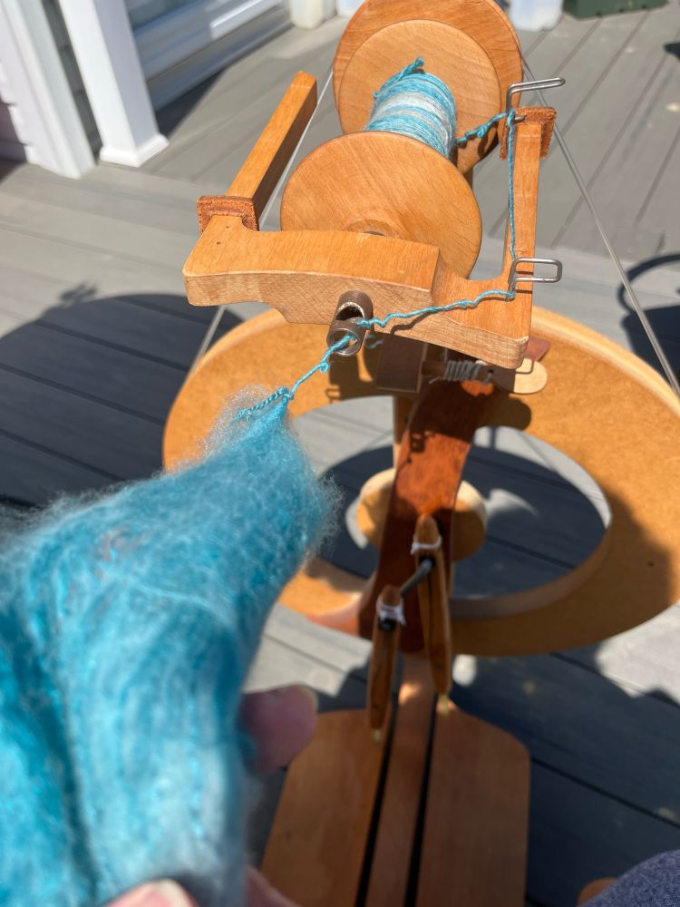 Blue fibers being spun into yarn on a wooden spinning wheel. 