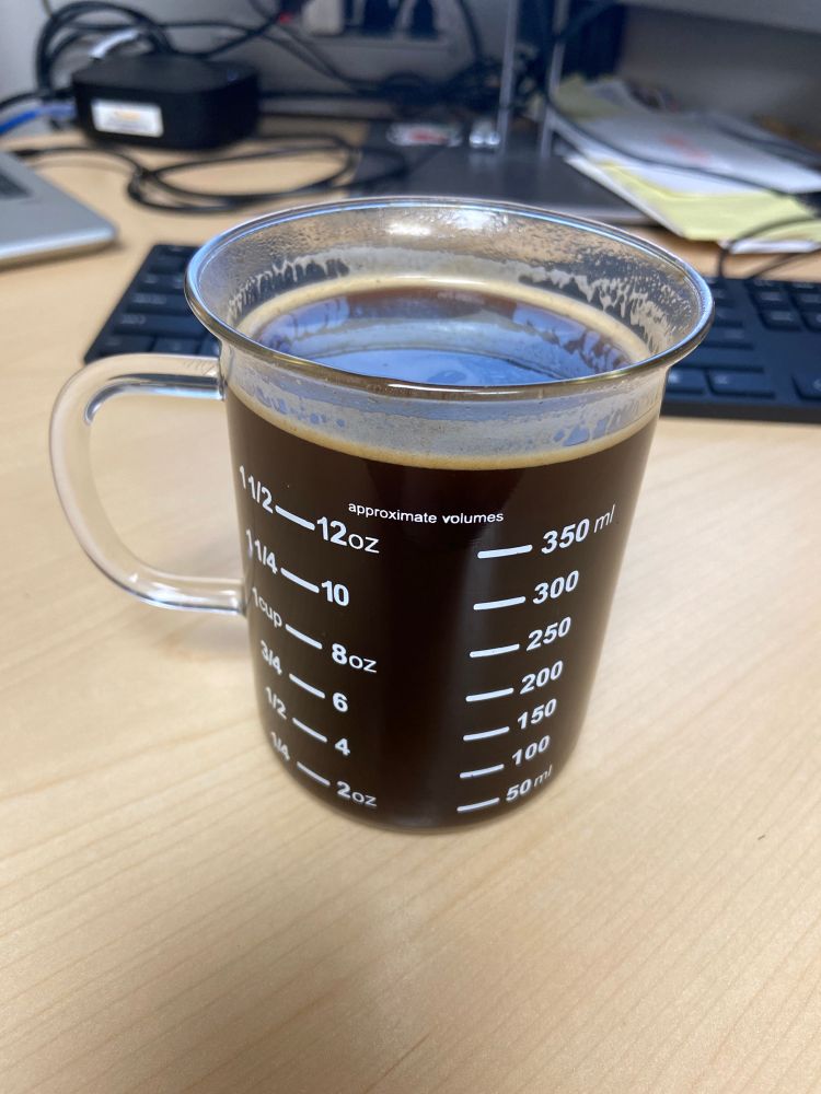 A picture of a beaker mug with both mL and Oz measurements on it. It is full of black coffee with a small amount of foam on the top.