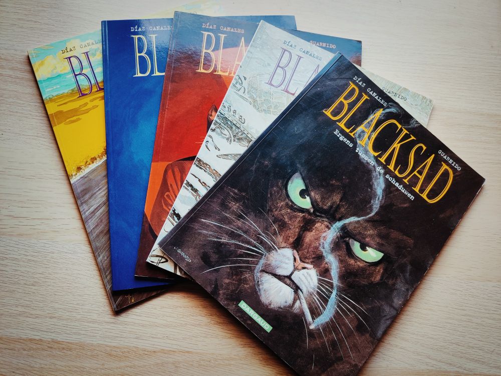 A collection of 'Blacksad' comic strips. The first and most visible one shows the face of Blacksad, an antromorphic cat smoking a cigarette.