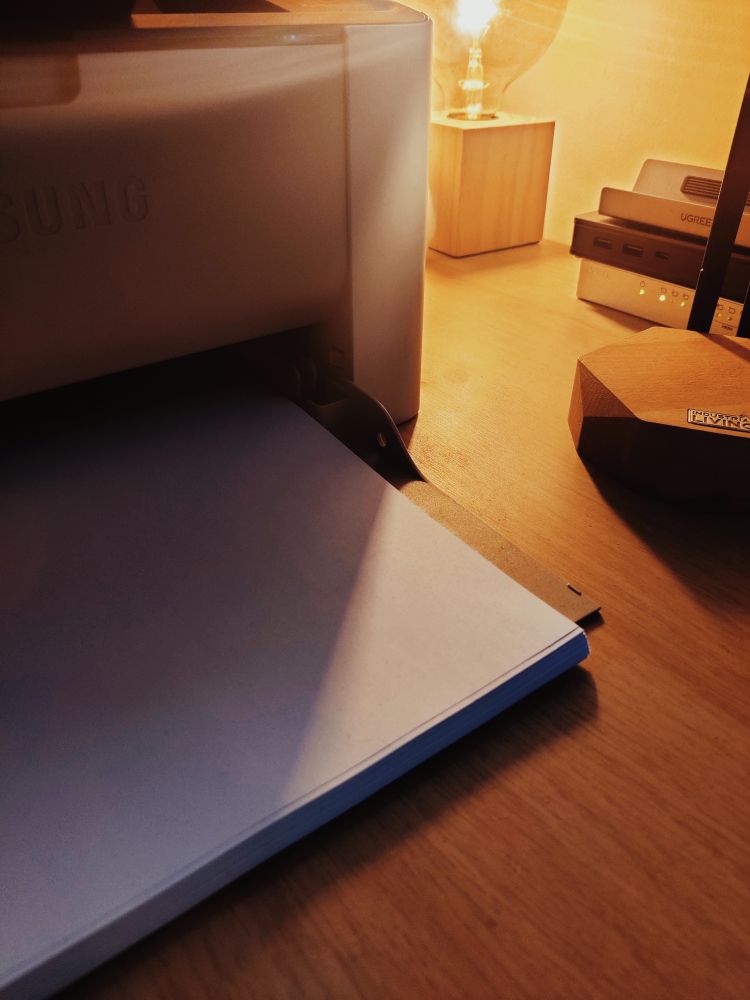 Moody shot of a desk featuring a printer, lamp and dome other paraphernalia...