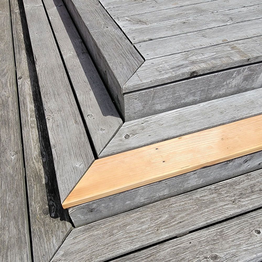 Faded wooden stairs with one plank replaced by a new one. 