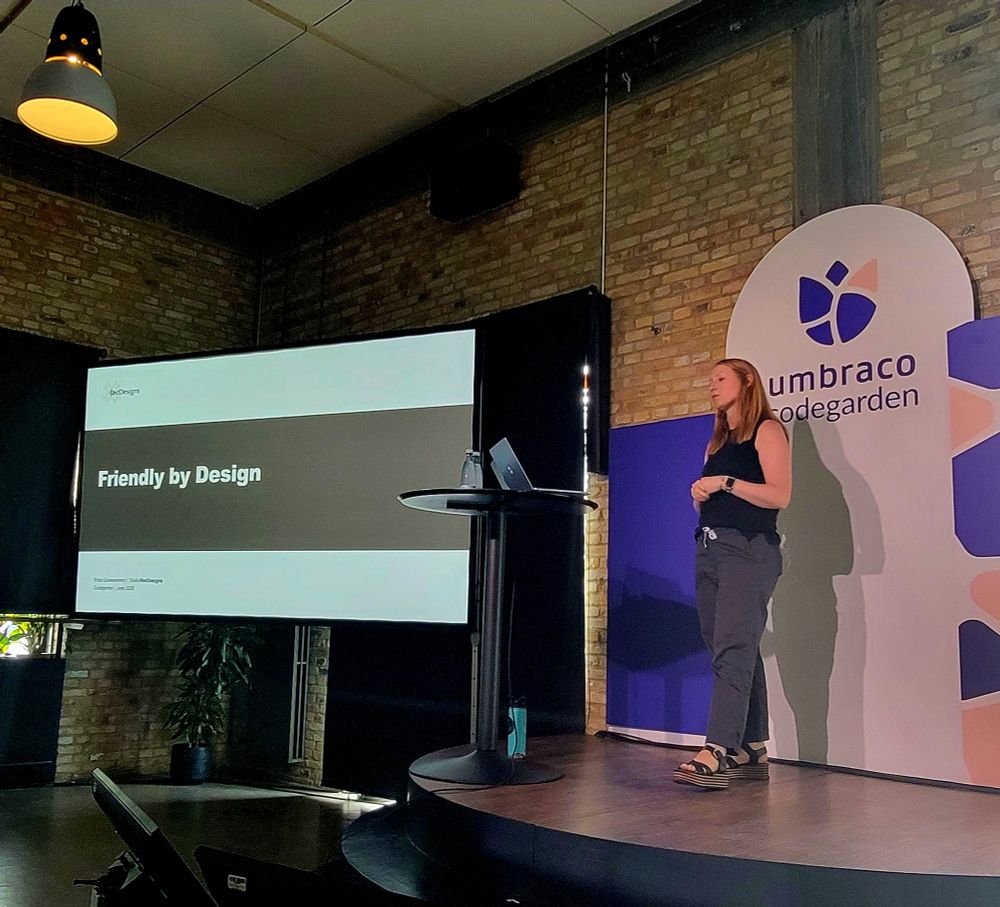 Erica Quessenberry standing on a stage at Umbraco Community giving her talk Friendly by Design. 