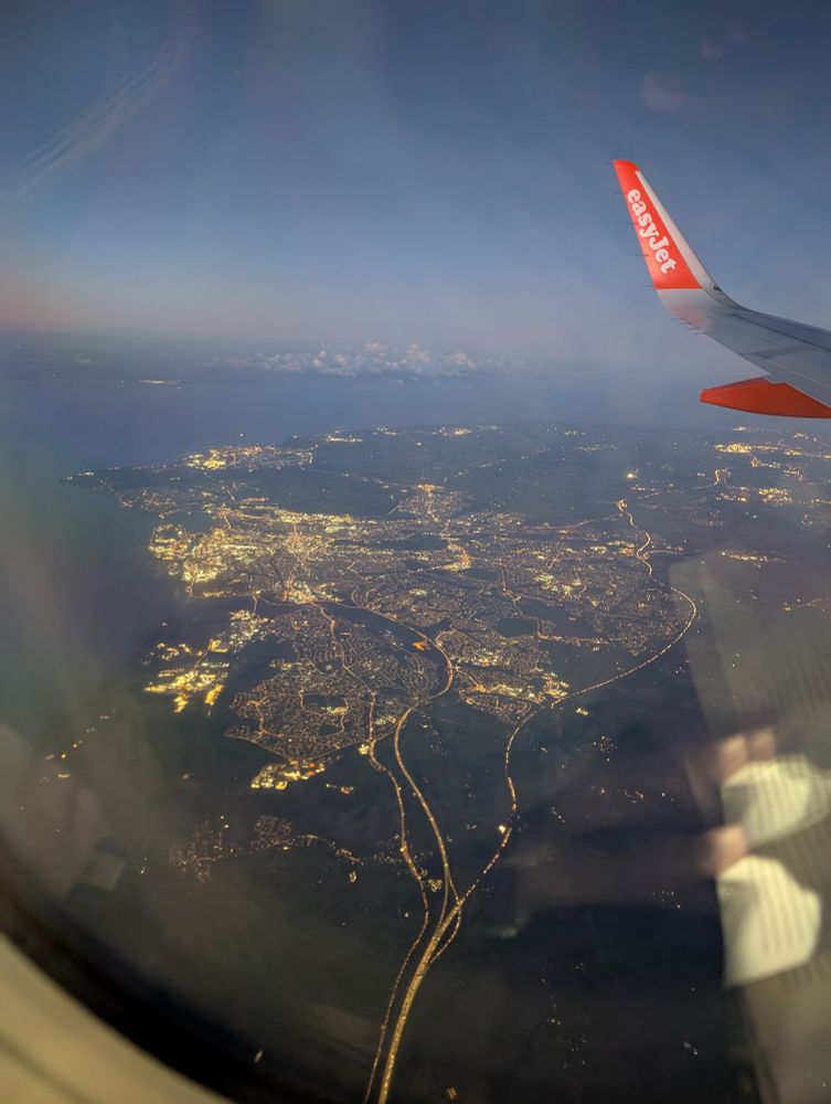 A view from a plane window of a lit up coastal city (Cardiff) in the early morning dawn