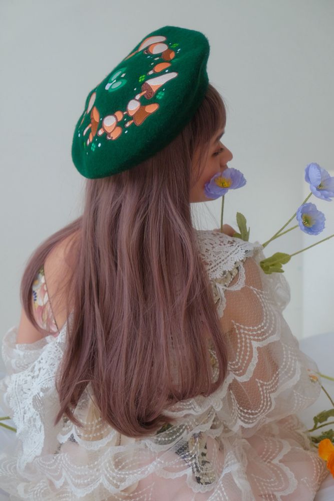 A model with long brown hair modeling a green felt beret with embroidered fairy ring on it. 
