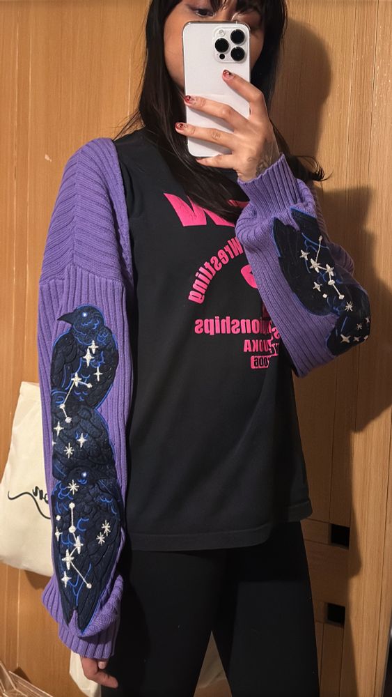 Person wearing purple rib knit bolero with crow embroideries on the sleeves. 