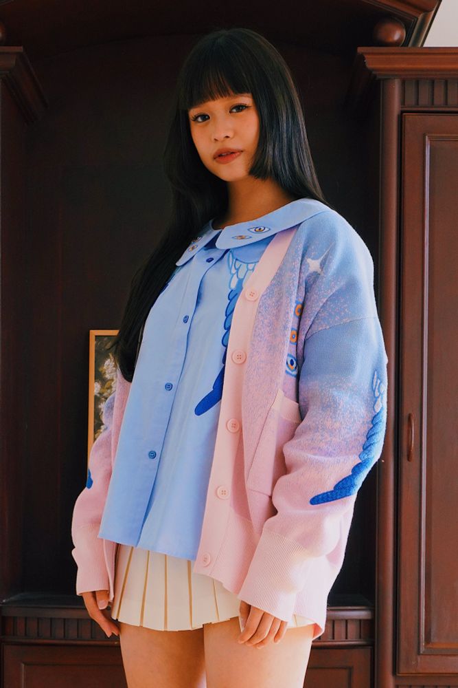 Model wearing blue peter pan collar shirt with blue eyes and wings embroideries with blue and pink gradient knit cardigan. 