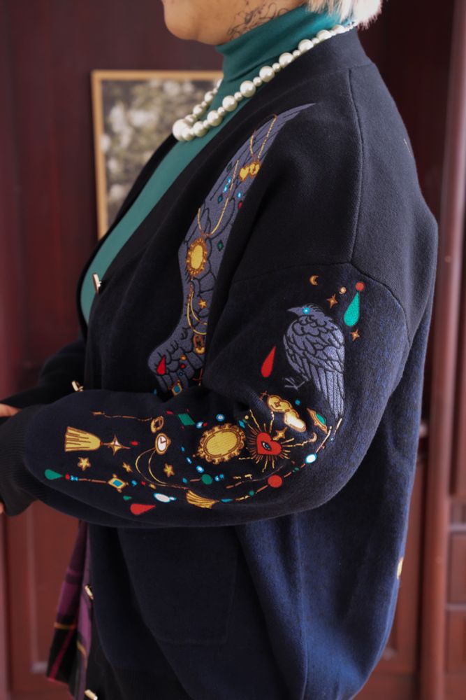 Model wearing black cardigan with colorful jewelry shaped embroideries. 