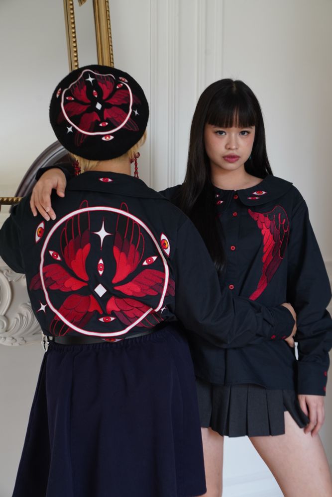Two models wearing black peter pan collar shirt with red eyes and wings embroideries on the front and collar, and eyes, wings, and halo embroideries on the back. 
