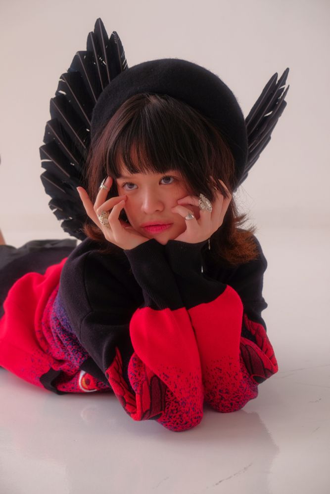 A model wearing black beret, black angel wings, and black and red cardigan with embroideries on the front and sleeves. 