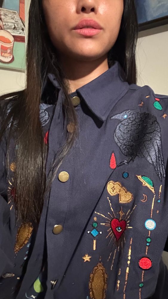 Person wearing navy blue jacket with crow and jewels embroideries. 