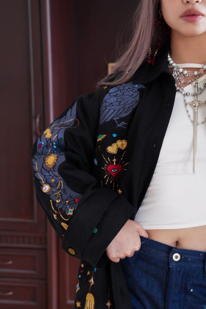 Model wearing black jacket with jewels and crow wing shaped embroideries. 
