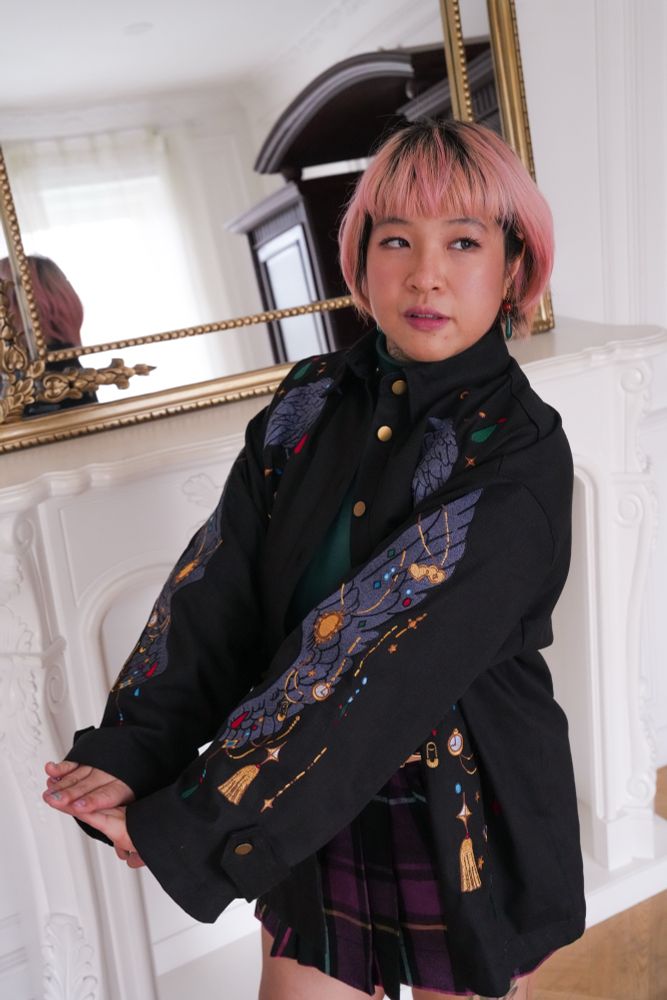 Model wearing black jacket with colorful jewelry shaped embroideries. 