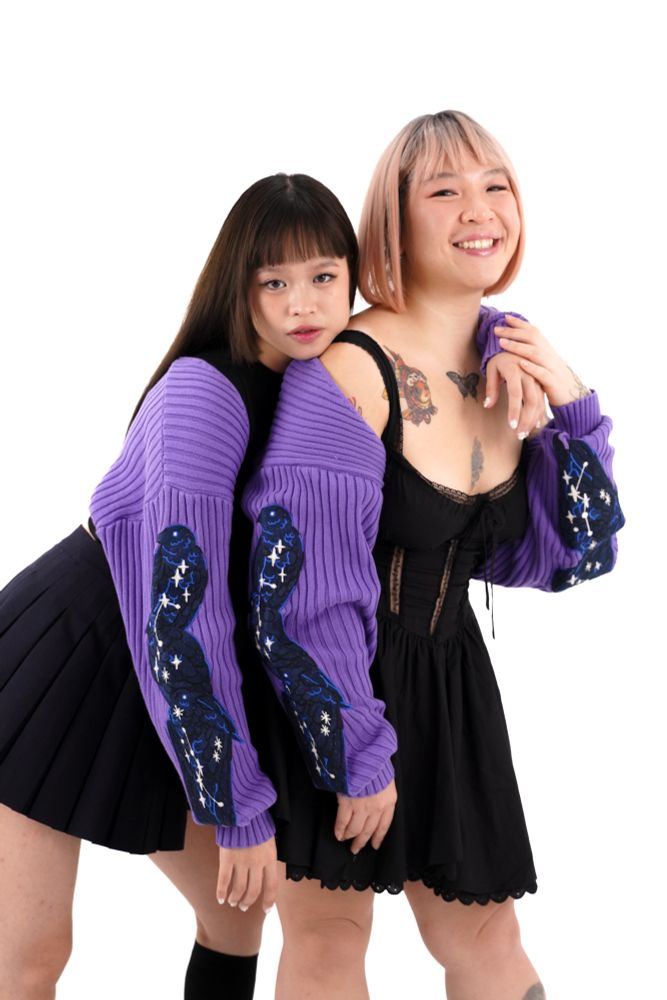 Two models wearing purple rib knit bolero with raven embroideries on the sleeves. 
