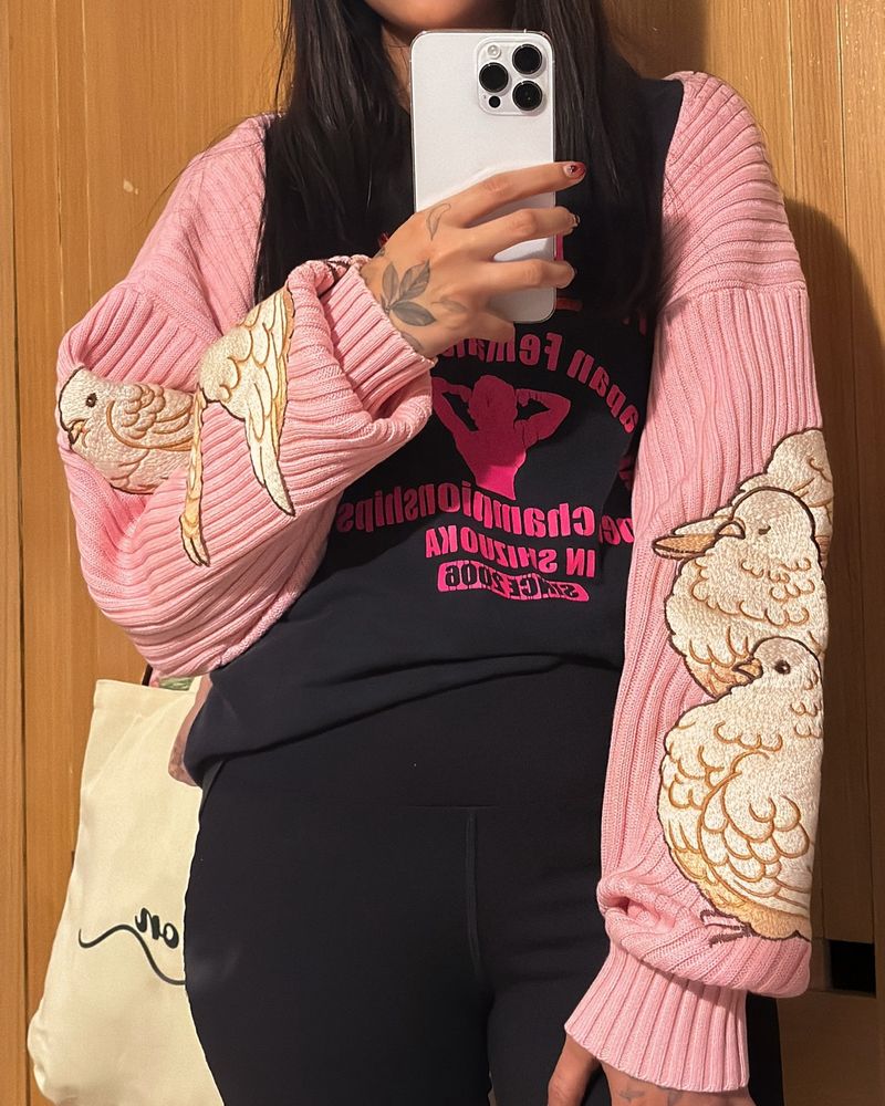 Person wearing pink rib knit bolero with pigeon embroideries on the sleeves. 