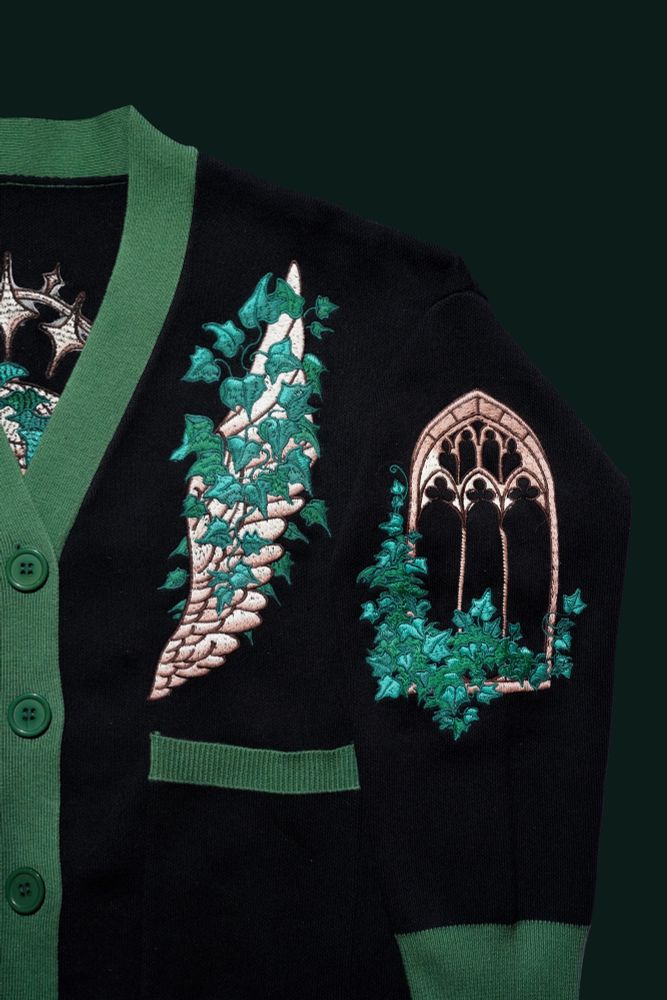 Black and green cardigan with embroidered angel wing and windows covered with ivy plant. 