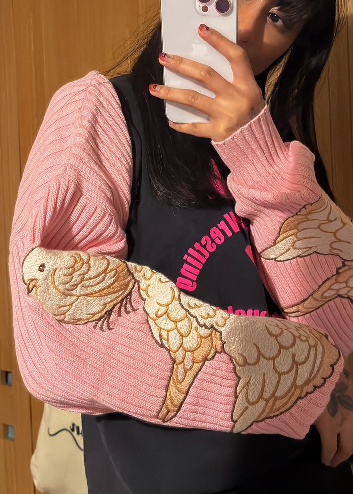 Person wearing pink rib knit bolero with pigeon embroideries on the sleeves.