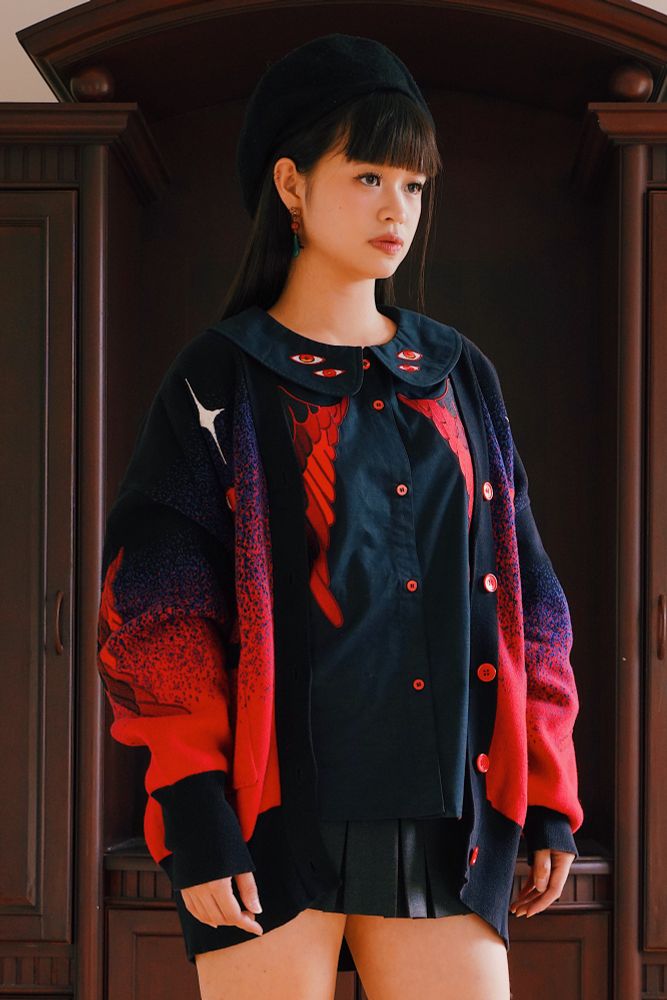 Model wearing black peter pan collar shirt with red eyes and wings embroideries with black and red knit cardigan. 
