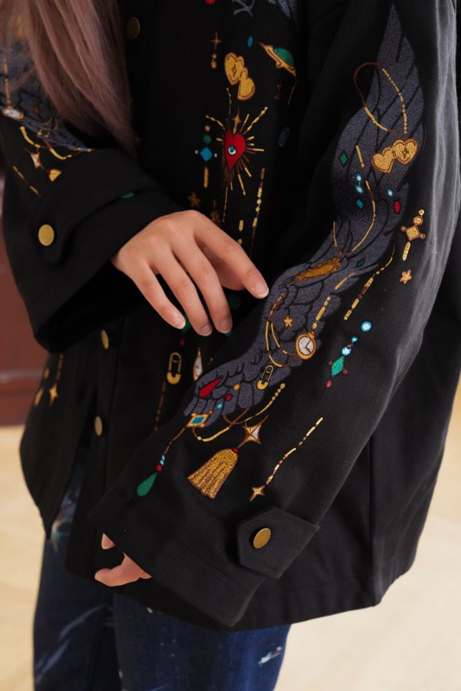 Close up photo of a model wearing black jacket with jewels and crow wing shaped embroideries. 

