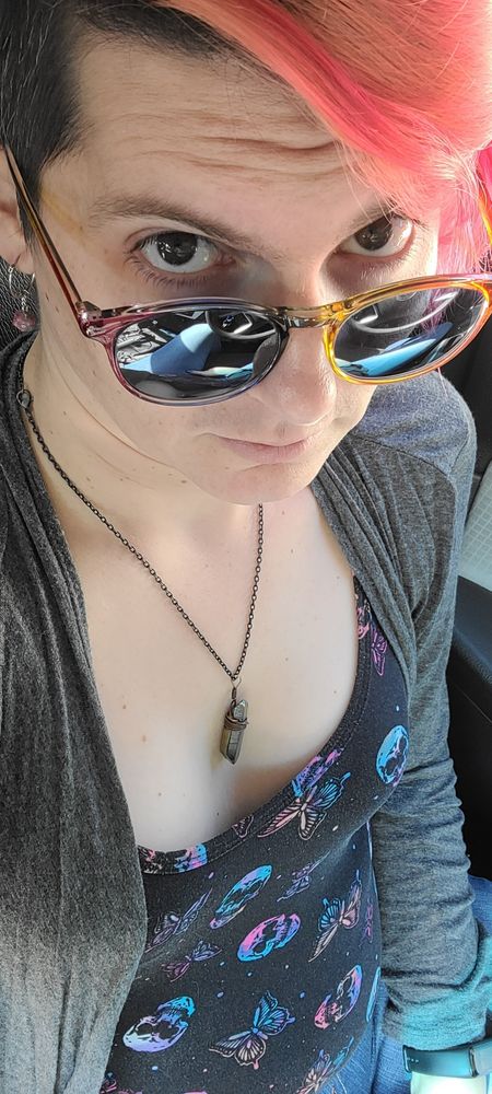 kay, a white genderfluid person, looking up into the camera over their sunglasses 