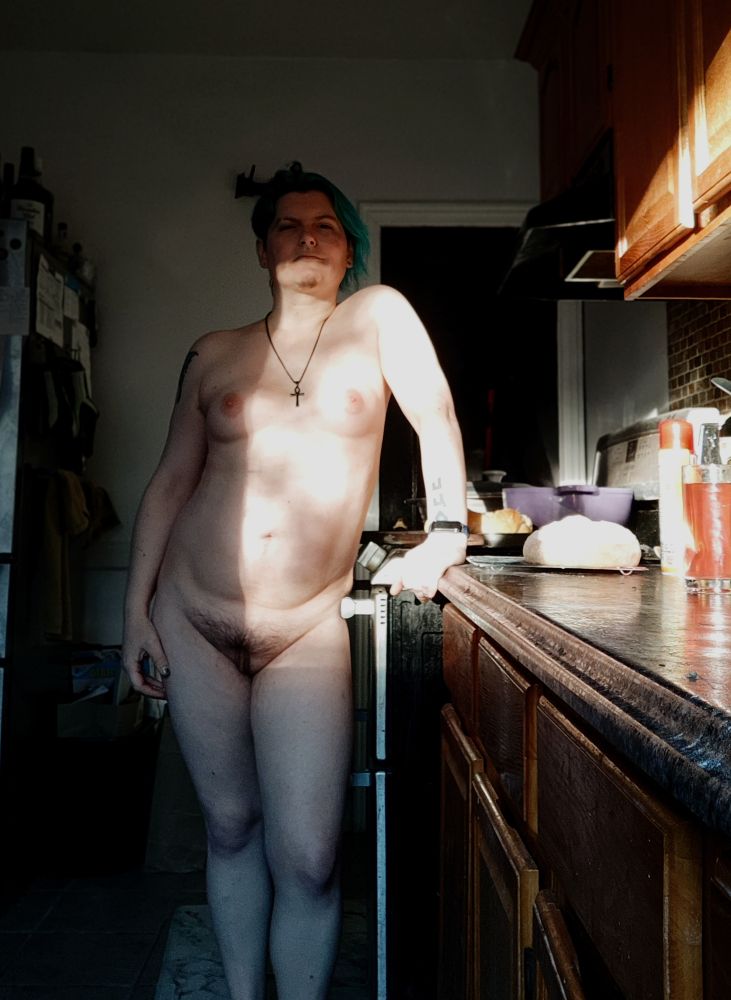 kay, a white genderfluid person, standing in a kitchen 