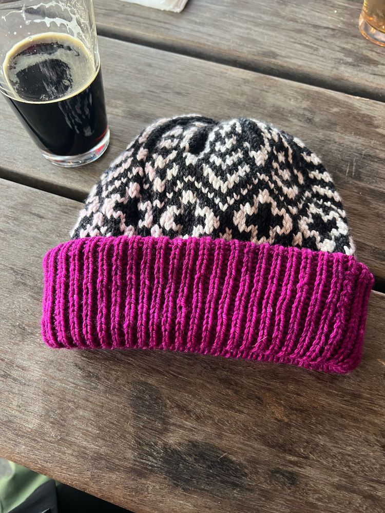 Beanie with black and white geometric shapes in stranded color work and a thick tri-fold fuchsia 1x1 rib brim.