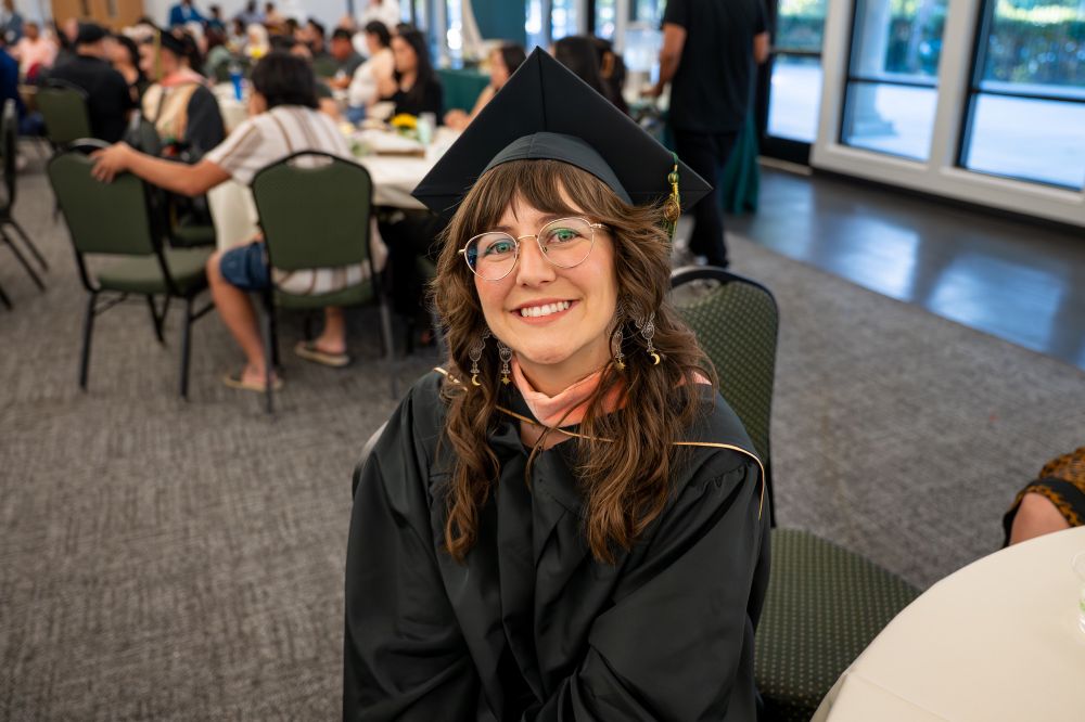 Smiling at my MPH graduation, wearing my cap and hood while seated at a table, proud and happy after two years of hard work.