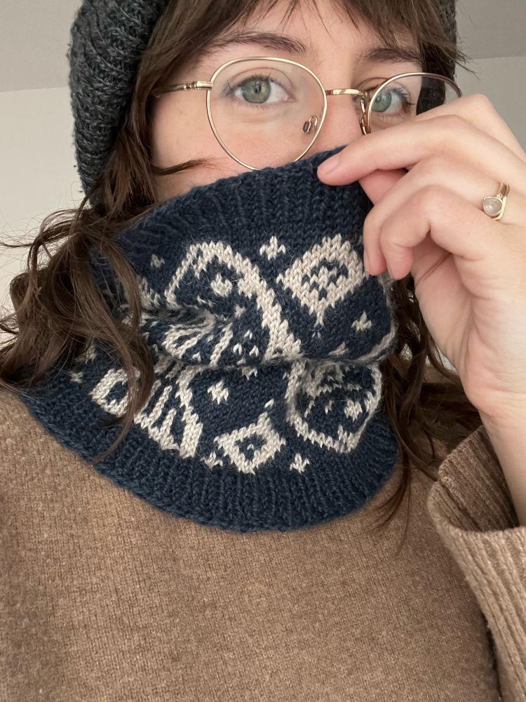 Dark blue neck warmer with light grey stranded color work. Color work design is obscured by being worn. 