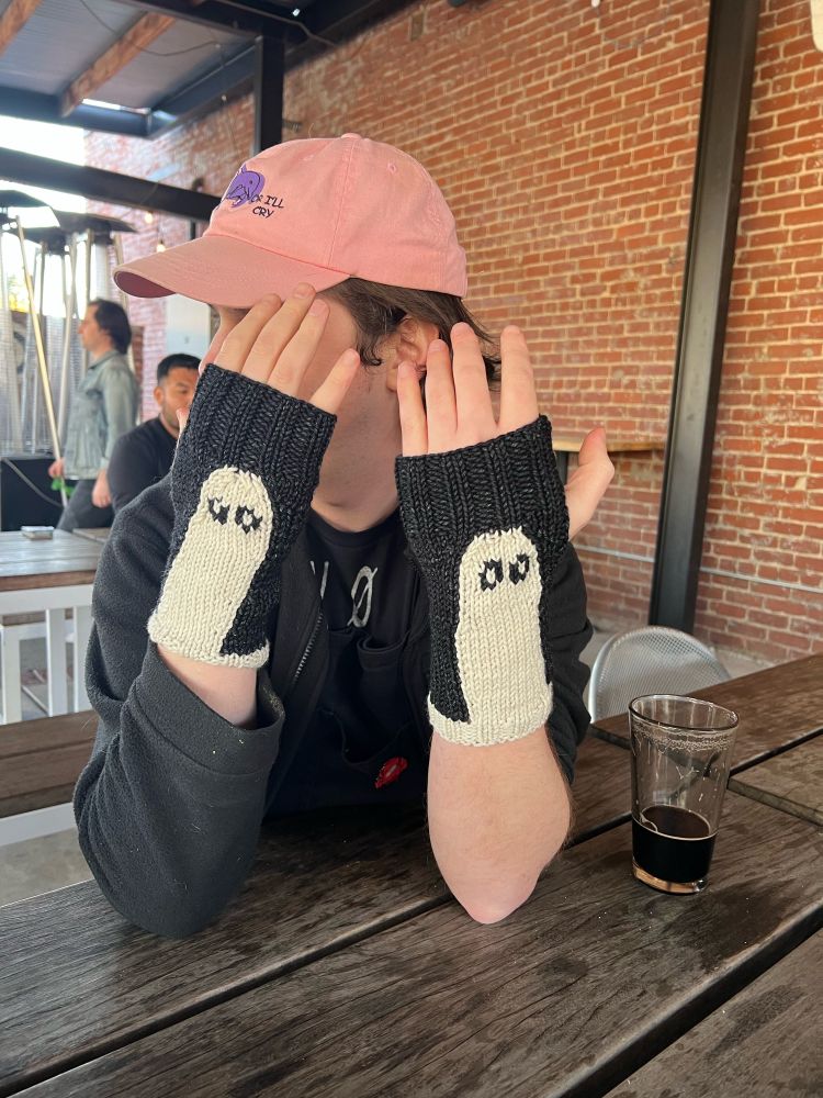 Black fingerless mitts with white intarsia ghosts on the back.