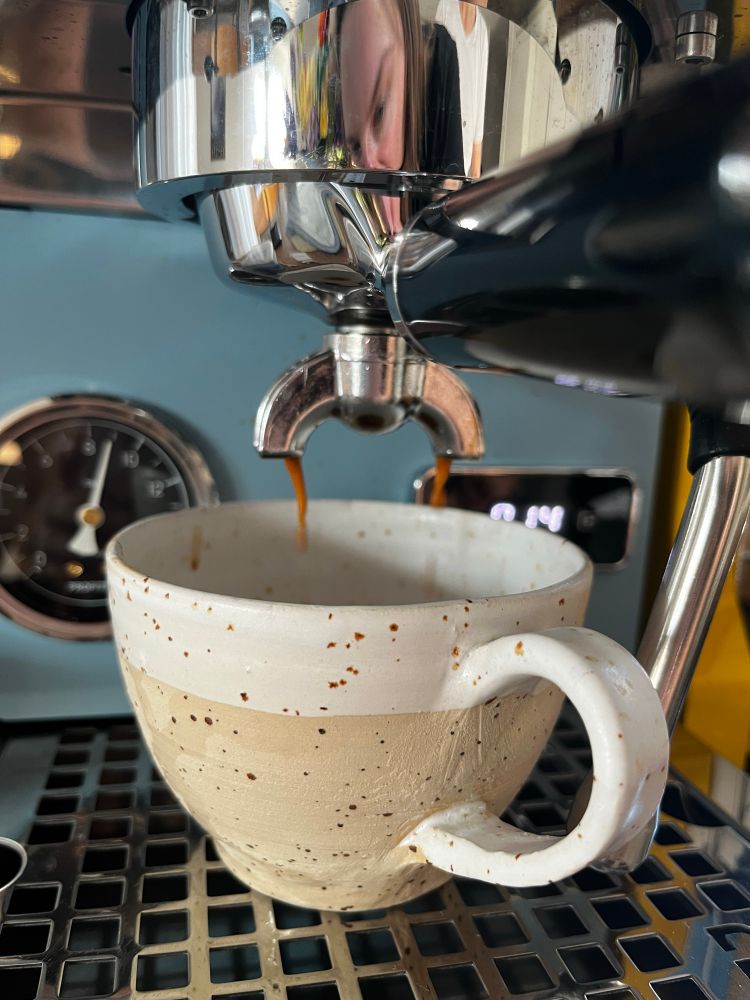 selbstgetöpferte Tasse unter einer hellblauen spiebträgermaschine es läuft Kaffe in die Tasse 